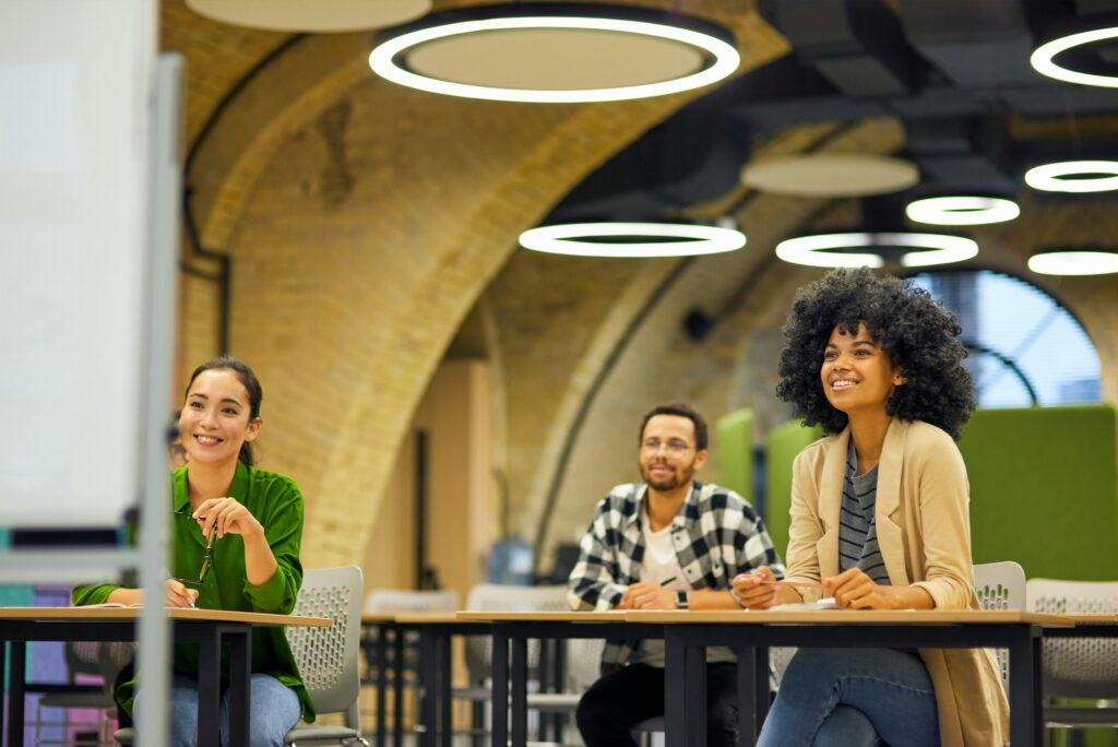 Group of young people sitting at desks in the modern office and listening to coach