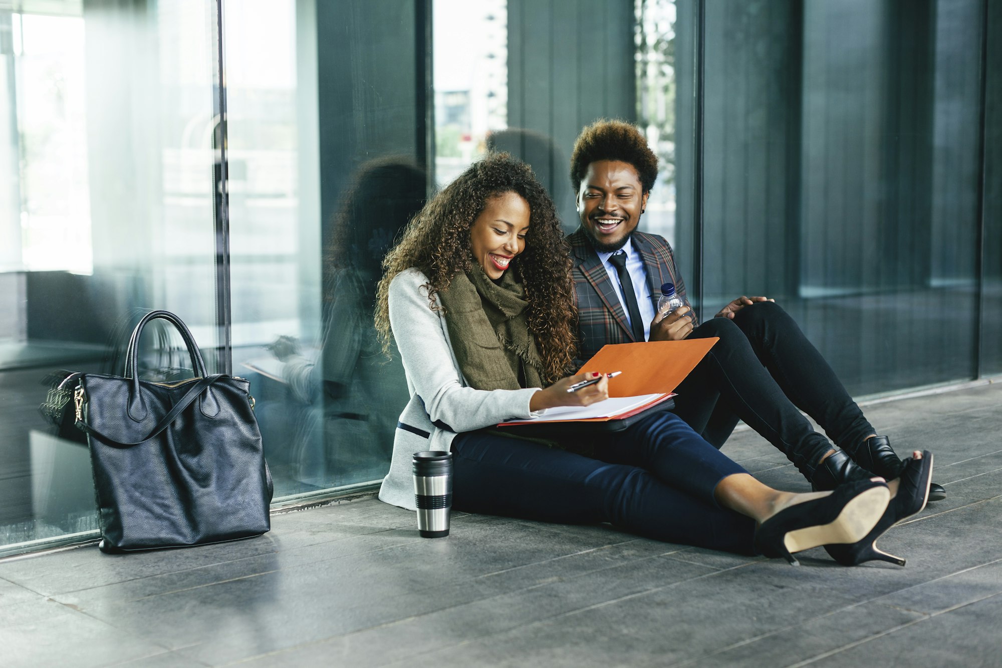 Two smiling young business people sitting on the ground with file